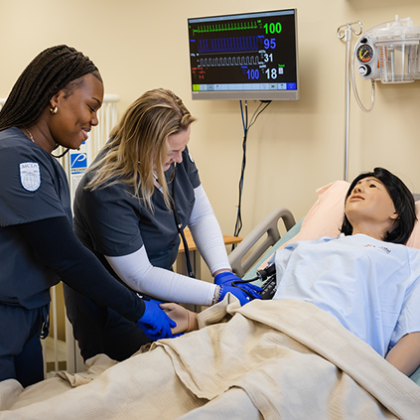Two Nursing students interacting with a simulation manikin.