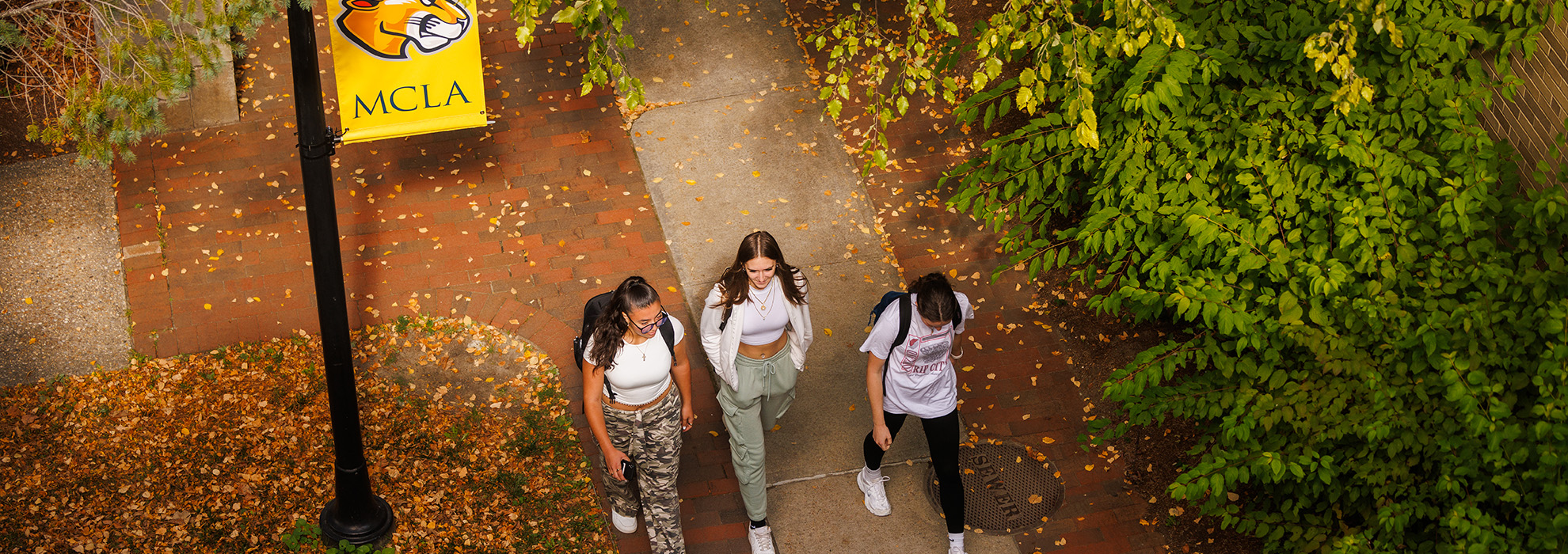 Three students walking across the MCLA campus with fall colors